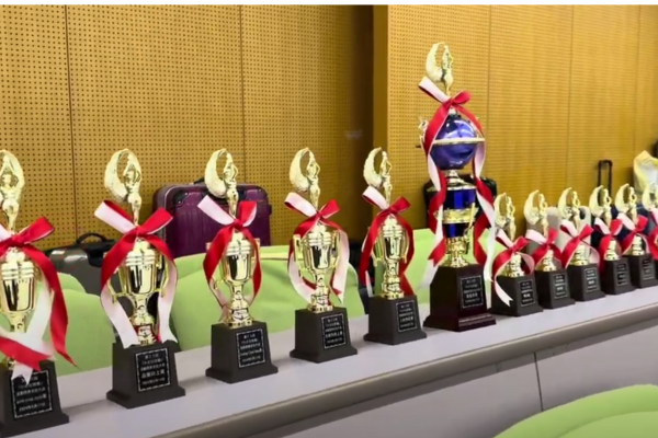 A row of golden trophies with red ribbons is lined up on a table, ready to be awarded to outstanding BPO services teams for their Kaizen initiatives and achievements.